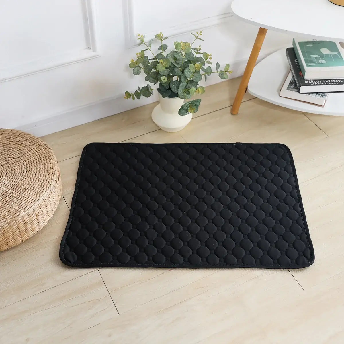 Black quilted dog cooling mat on wooden floor, ideal for hot days, washable, reusable, extra absorbent, and waterproof exterior.