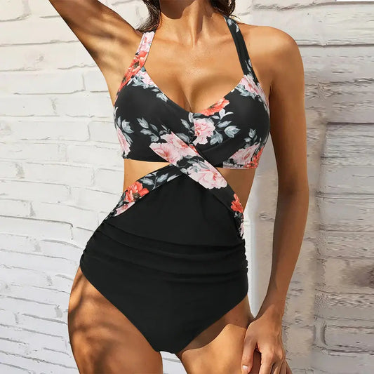 Woman wearing a floral one-piece swimsuit with cutout design against a white brick wall.